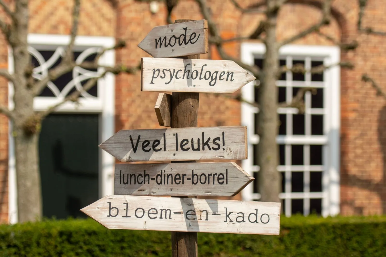 A rustic wooden signpost in a city, featuring Dutch text against a brick building facade.